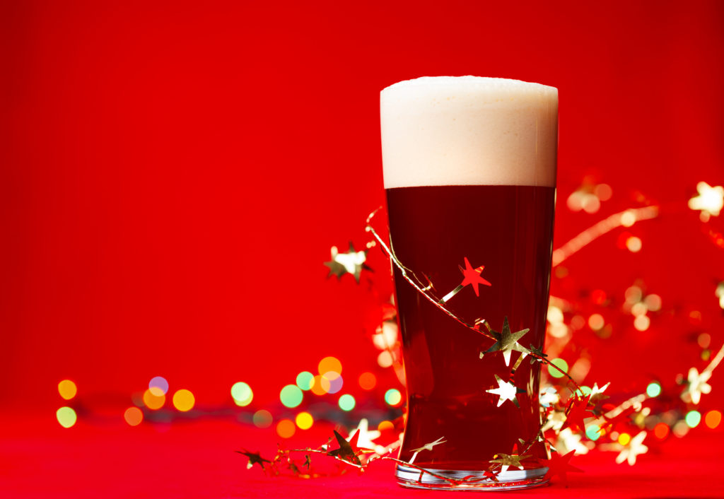 Full glass of bear or ale with tinsel and christmas lights on red background