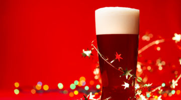 Full glass of bear or ale with tinsel and christmas lights on red background